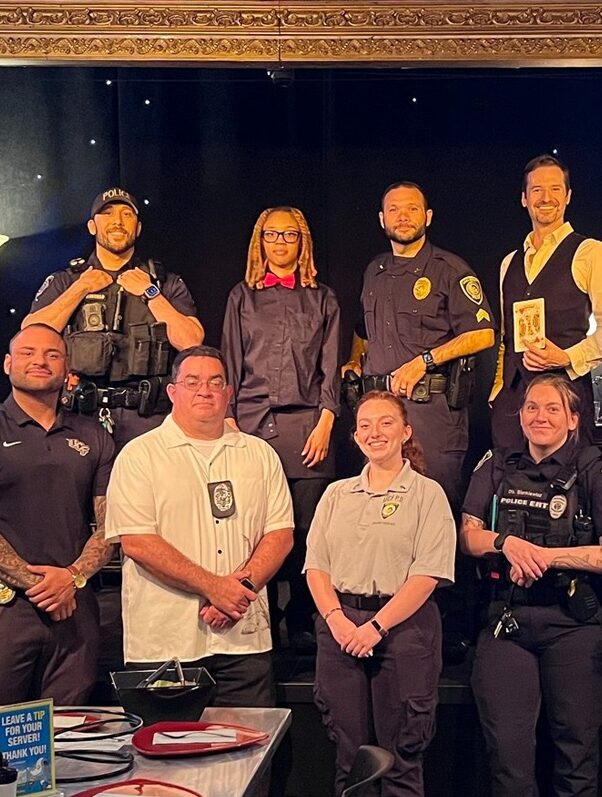 Fourteen people including police officiers, exploreres and community members posing in front of a stage