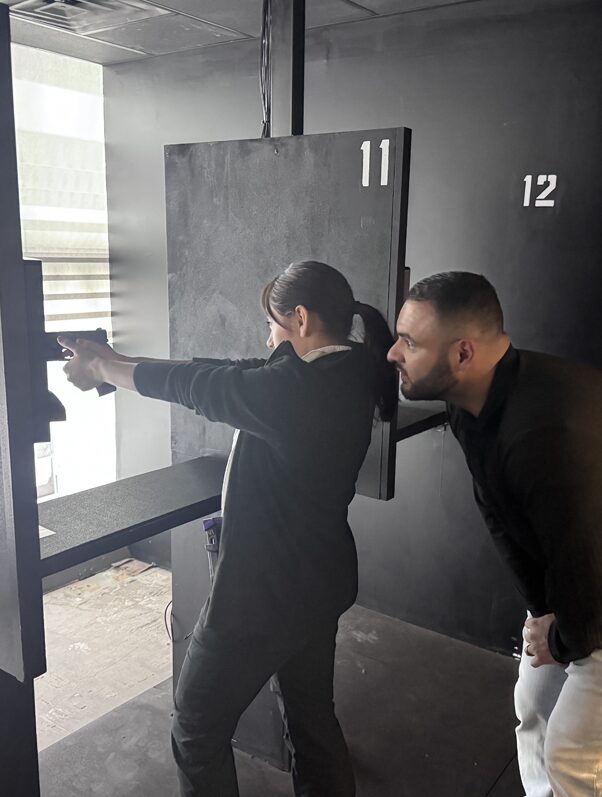 A female explorer firing a handgun inside a shooting range with a police officer supervising