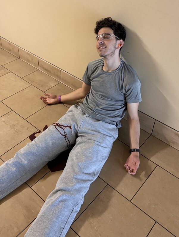 A person lying on the ground with an open wound on his left leg.