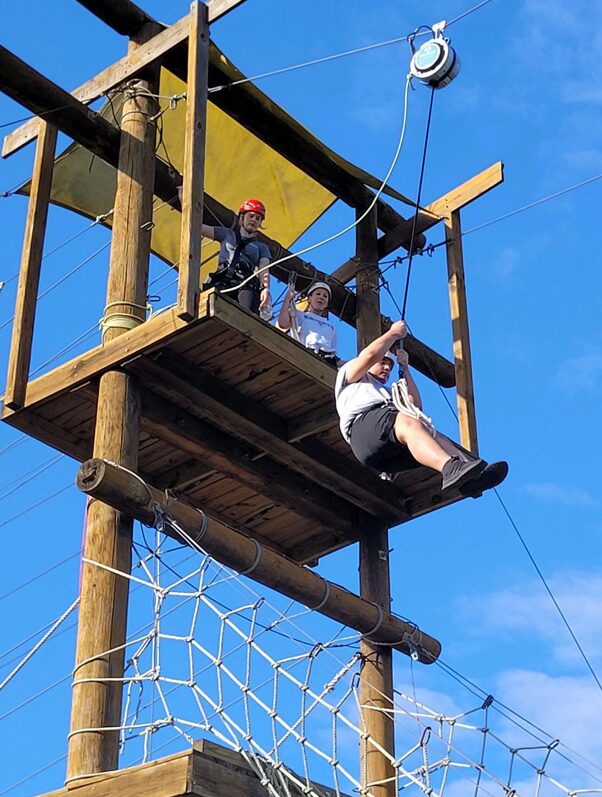 A person repelling from a wooden tower as two other explorers watch.